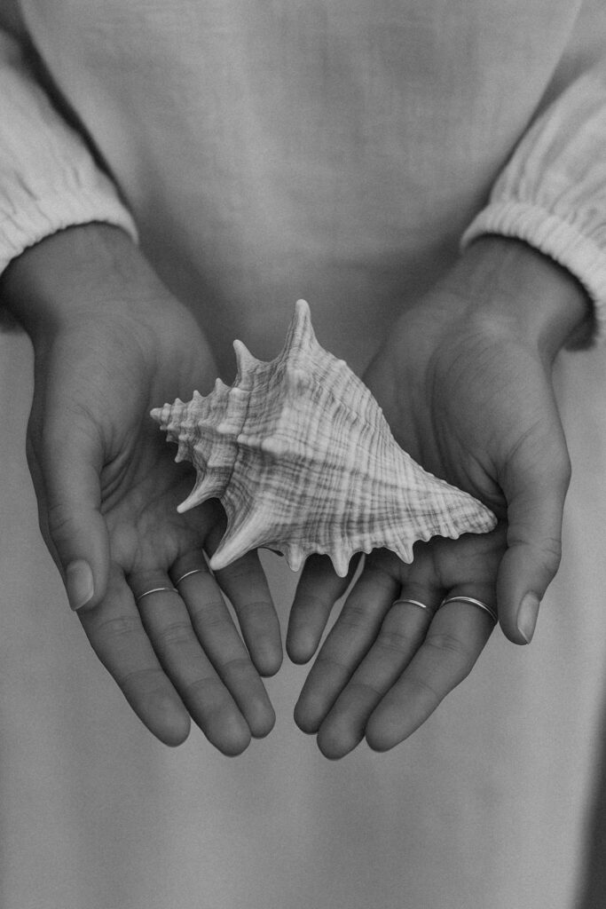 Black and white close-up of a womanâ€™s hands gently holding a seashell. The image has a minimal and intimate tone. It evokes calm, feminine energy and coastal simplicity. Suitable for wellness brands, lifestyle visuals, or editorial storytelling. Created with the assistance of AI tools.